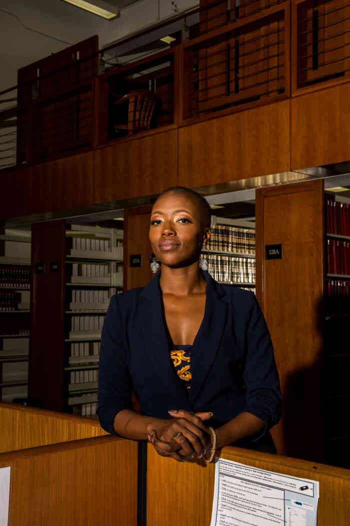 Portrait of a bald Black woman confidently standing in a legal library.